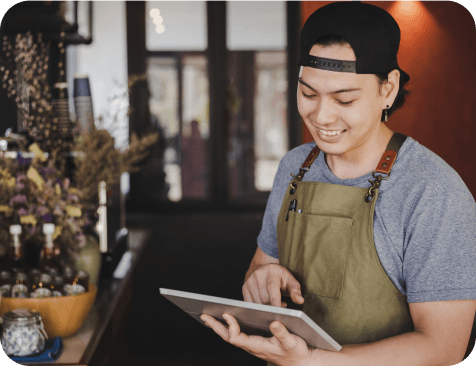 A waiter with an apron works with a tablet and smiles at the same time.