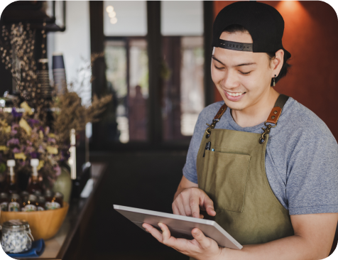 A waiter with an apron works with a tablet and smiles at the same time.