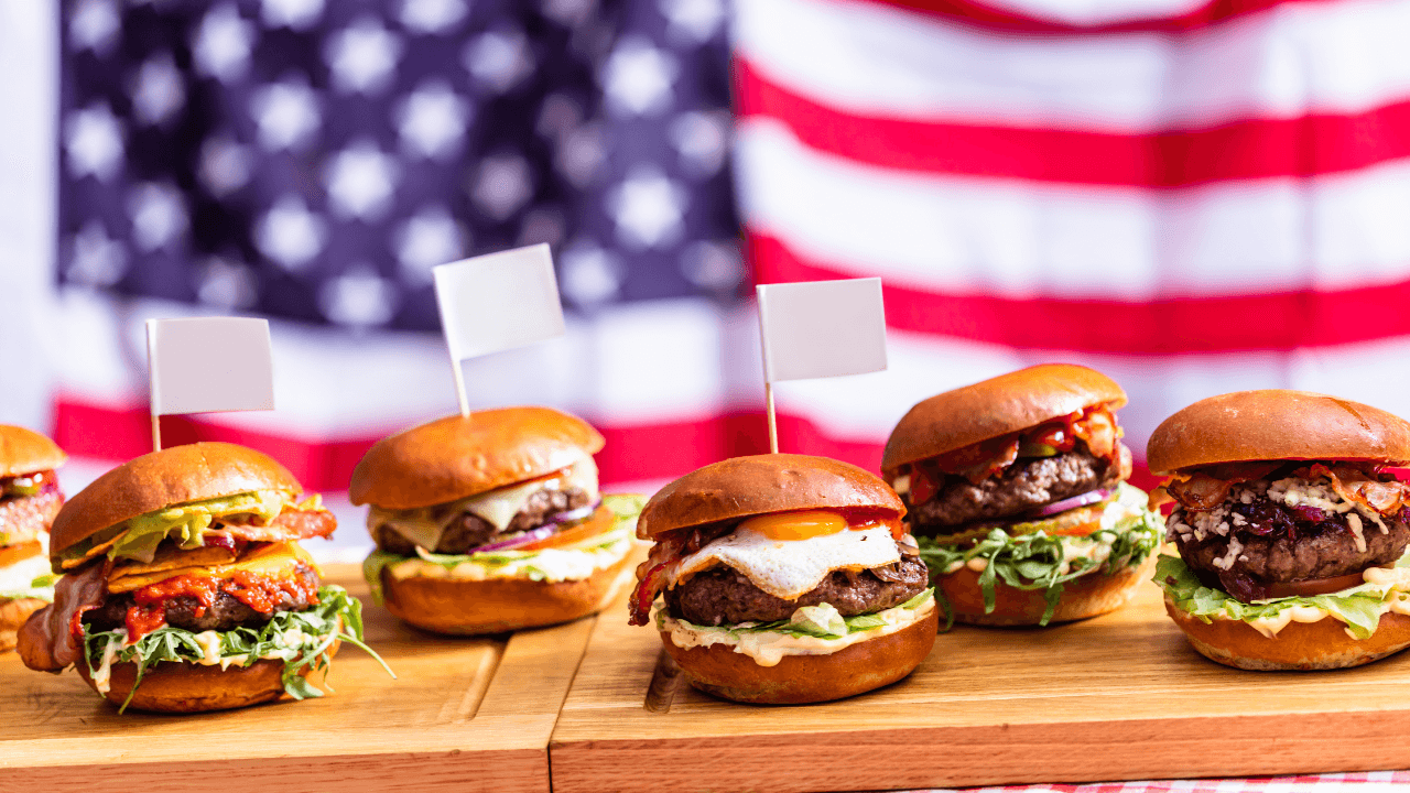 6 burgers, placed next to each other on the wooden board American flag in the background.