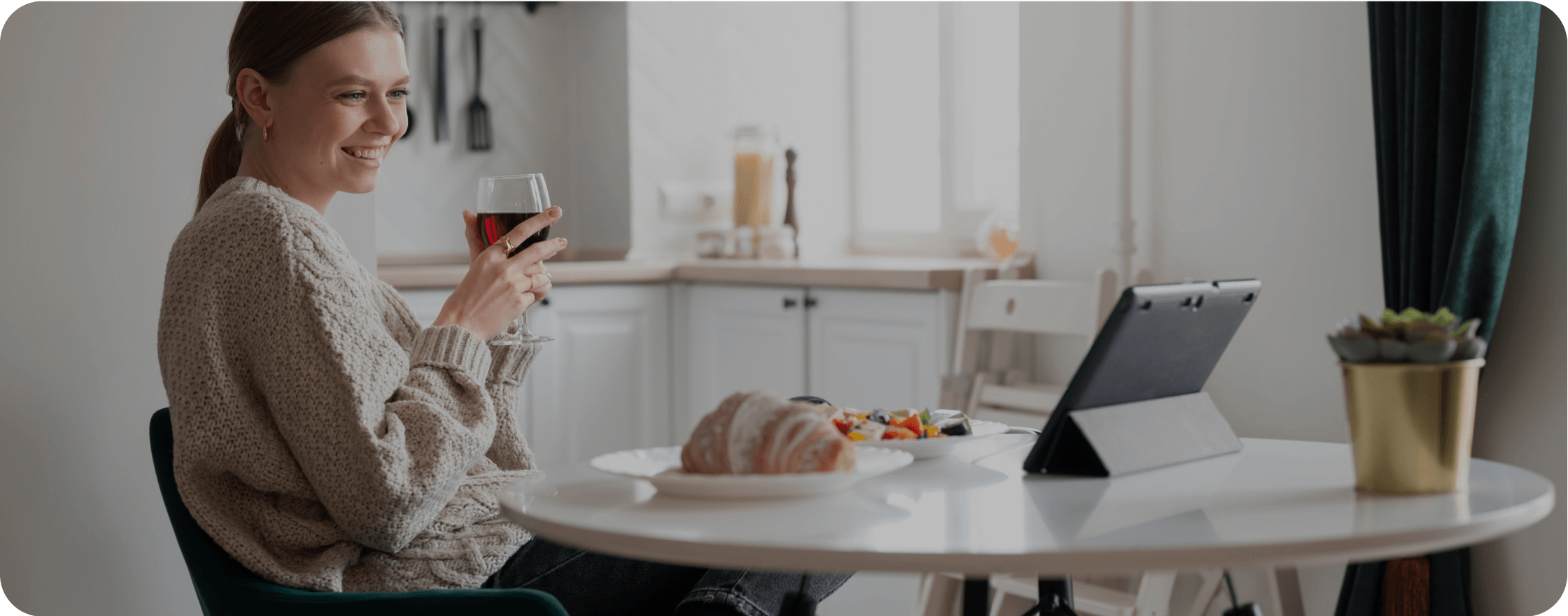 A girl, with a glass of wine in her hand, is having breakfast and looking at the tablet.