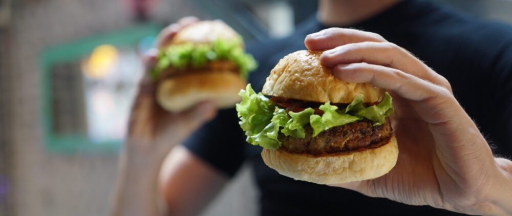 A young man holds two burgers with both of his hands.