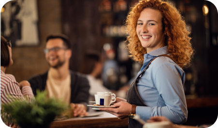A waiter holds cups of coffee and smiles at the camera.