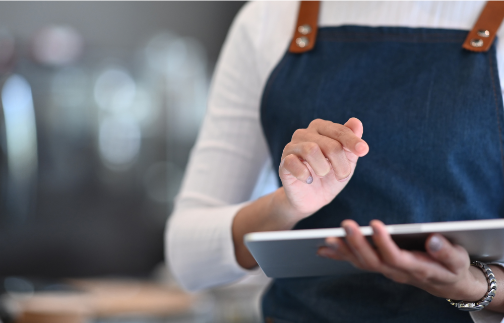A waiter on an apron is working with a tablet.