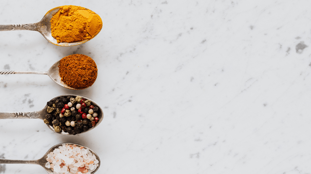 Assorted spices on white marble with spoons.
